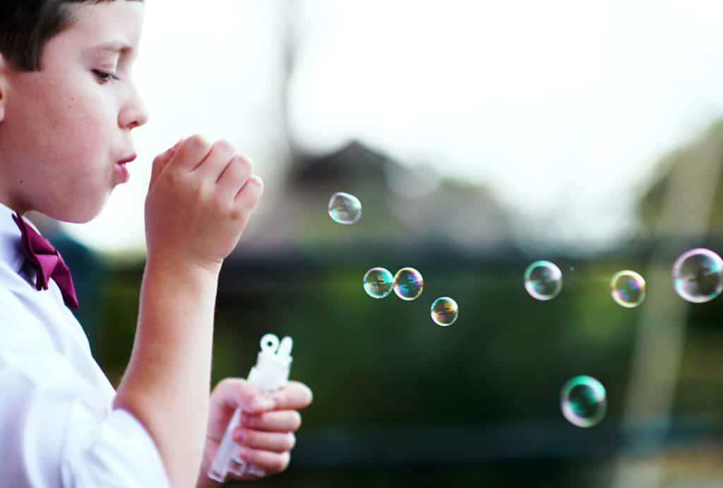 niño con corbatín rojo soplando burbujas.