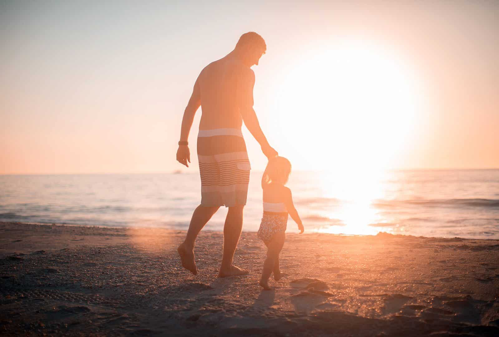 padre llevando de la mano a su hija de 2 años hacia el mar amorosamente